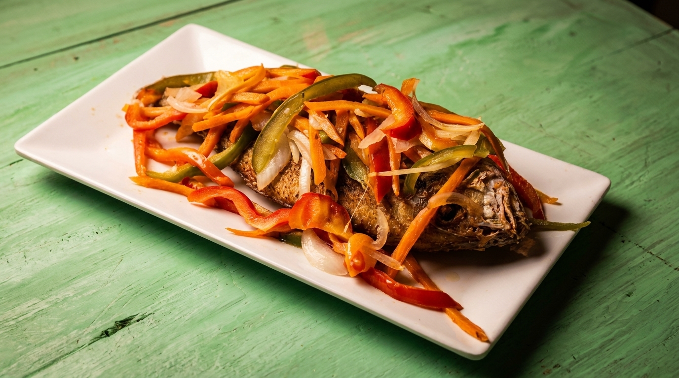 Whole fried fish topped with sautéed red and green peppers, carrots, and onions on a white plate.