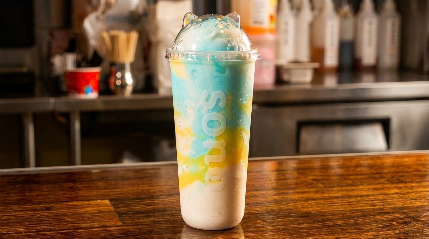 A colorful Sono drink with blue, yellow, and white layers sits on a wooden counter.