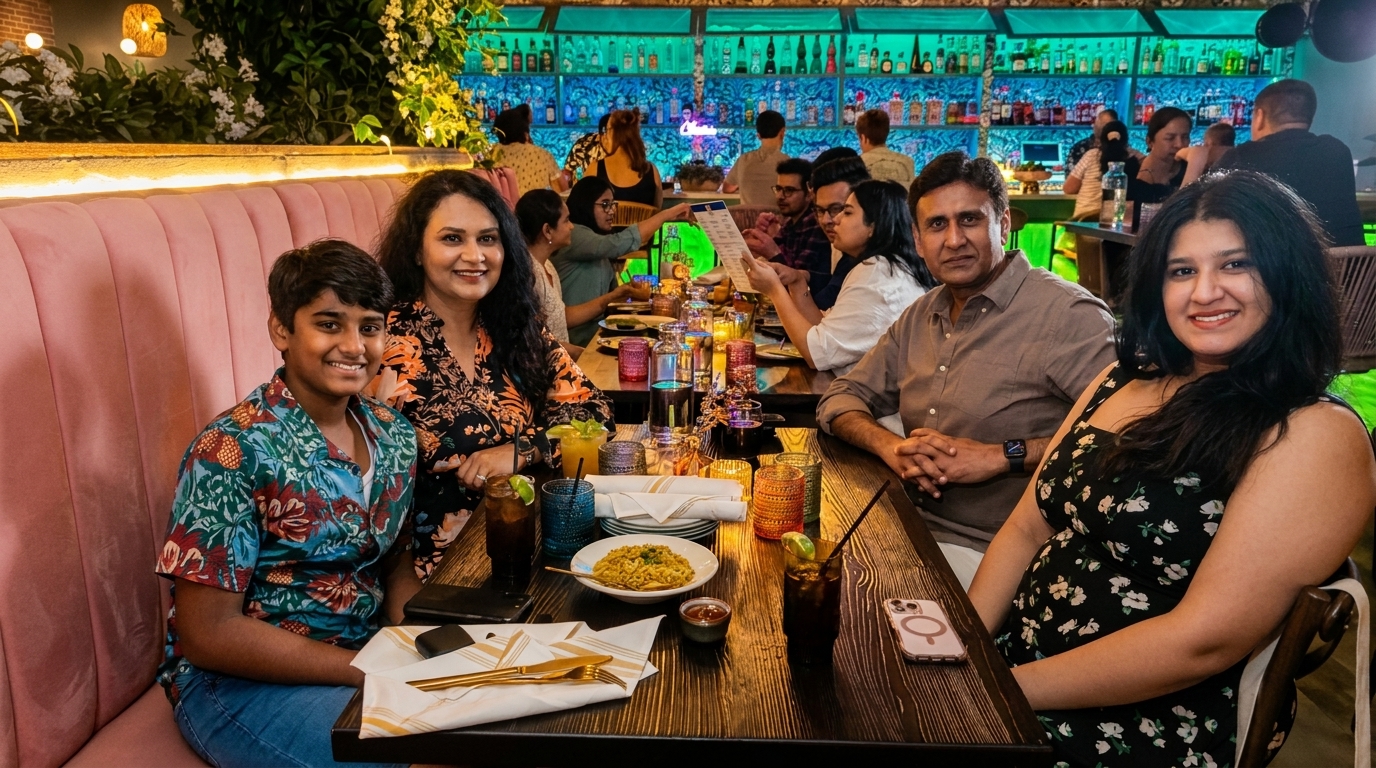 A family of four smiling at the camera, seated at a table in a vibrant, dimly lit restaurant.