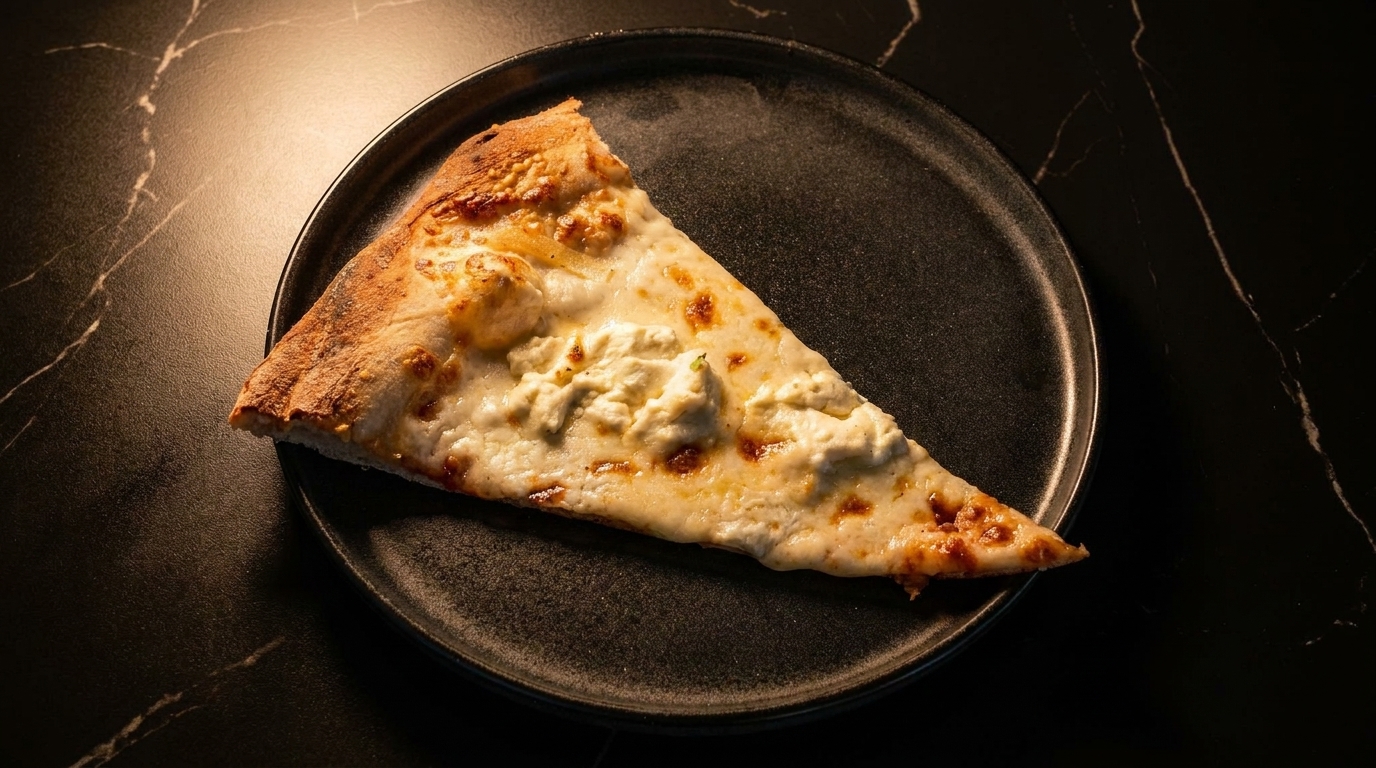 A single slice of white pizza with ricotta cheese on a dark plate, on a black marble table.