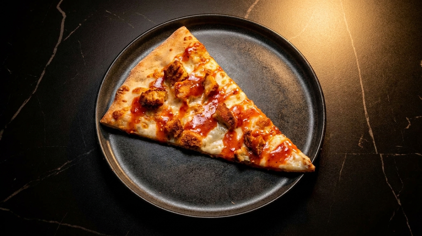 A single slice of buffalo chicken pizza with red sauce and cheese on a dark plate.