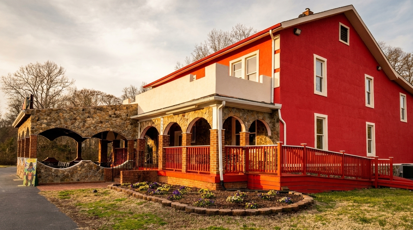Exterior of a red building with a stone archway, red railings, and a flower bed.