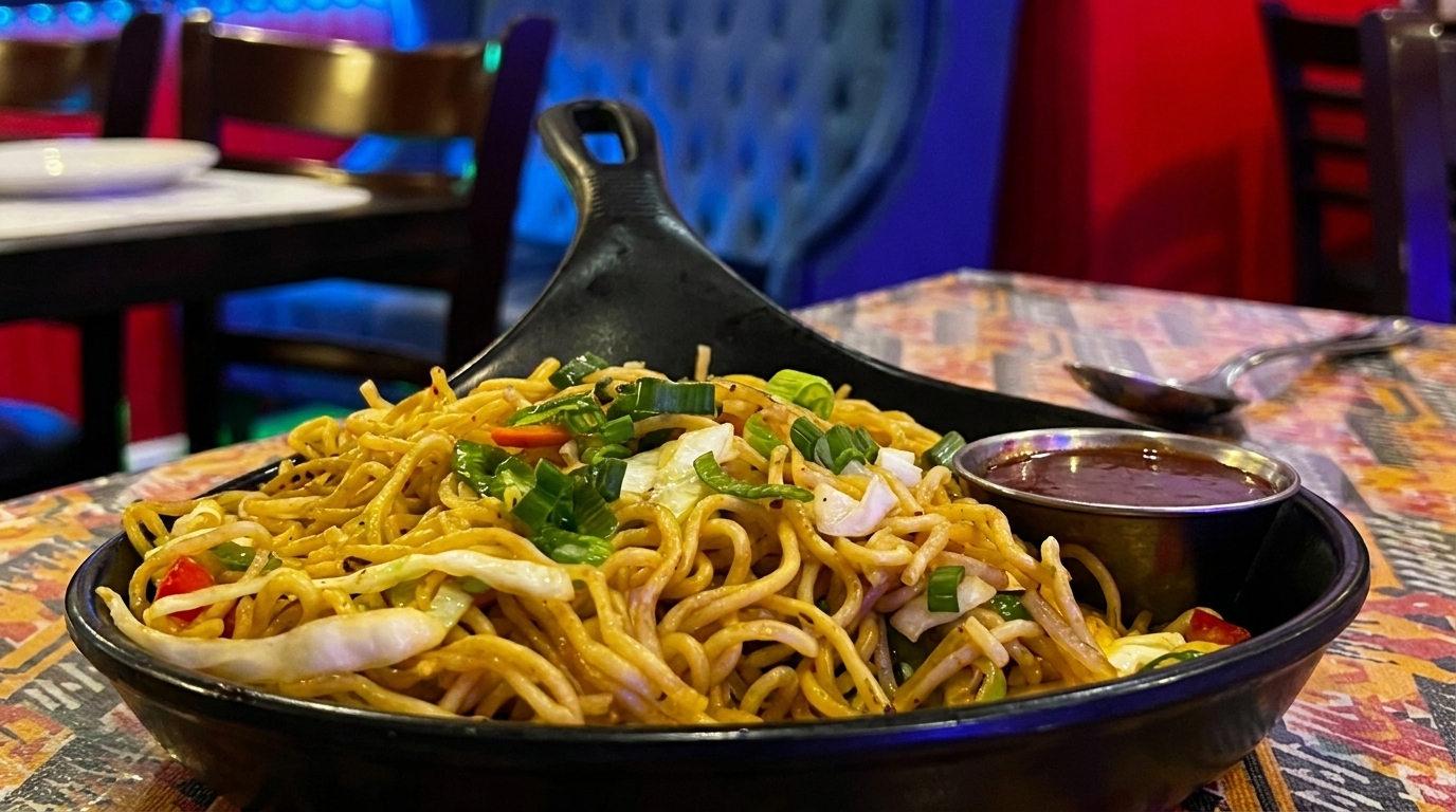 Noodles with vegetables and green onions in a black bowl with a side of sauce.
