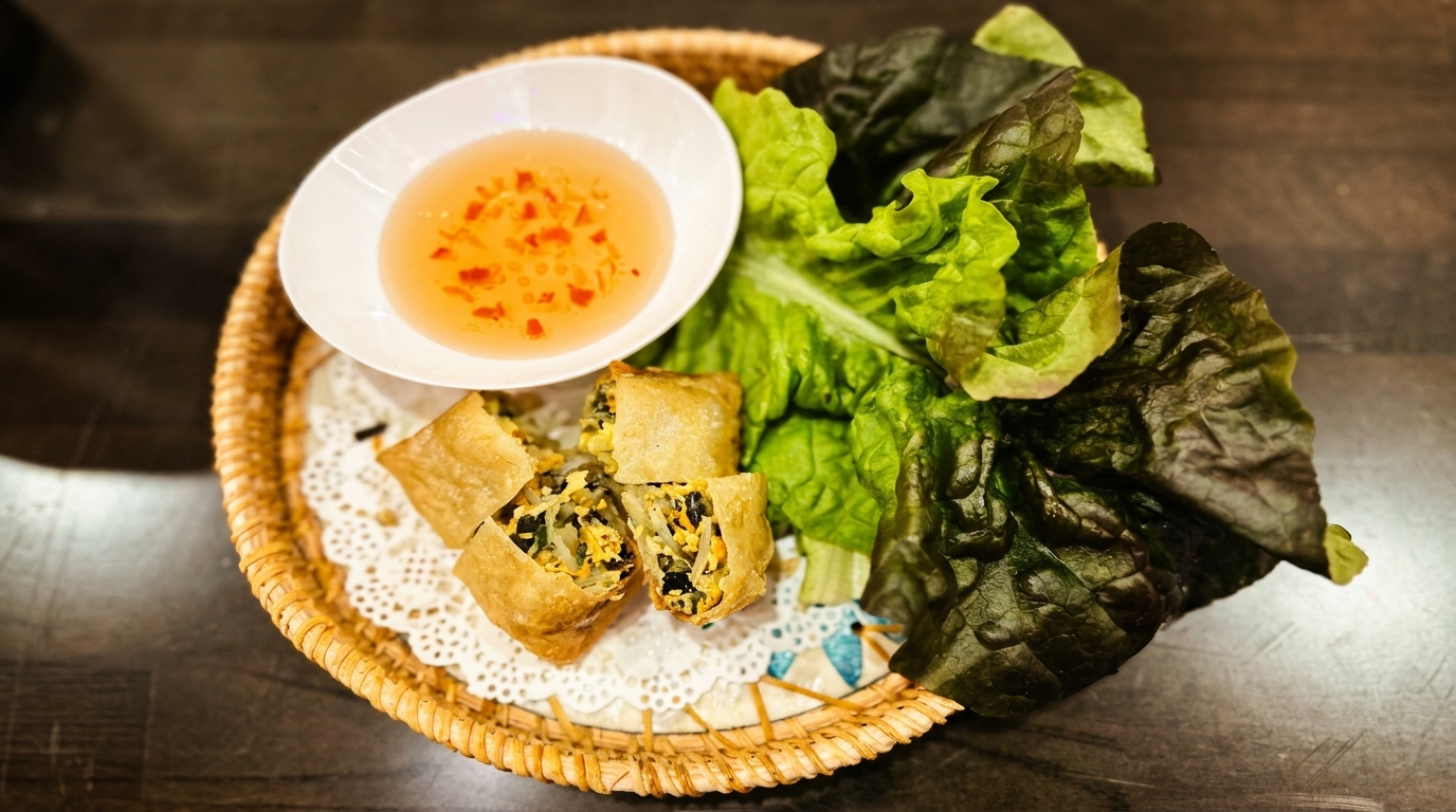 Crispy fried spring rolls, lettuce, and a dipping sauce in a woven basket on a dark table.