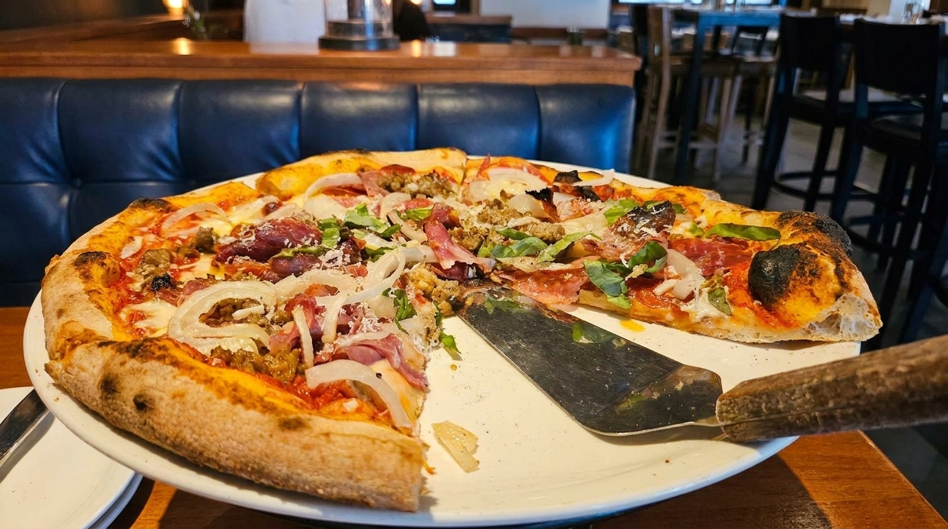 A large, partially eaten pizza with various toppings and a metal server on a white plate.