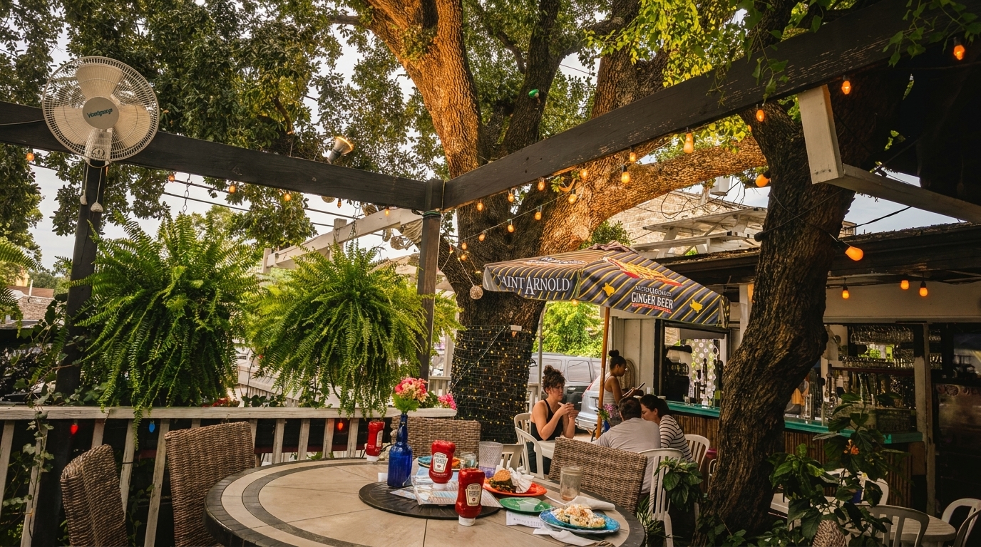 Outdoor restaurant patio with diners, large trees, string lights, and hanging ferns.