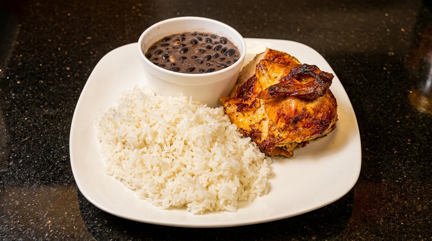 Grilled chicken with white rice and a side of black beans in a white cup on a black countertop.