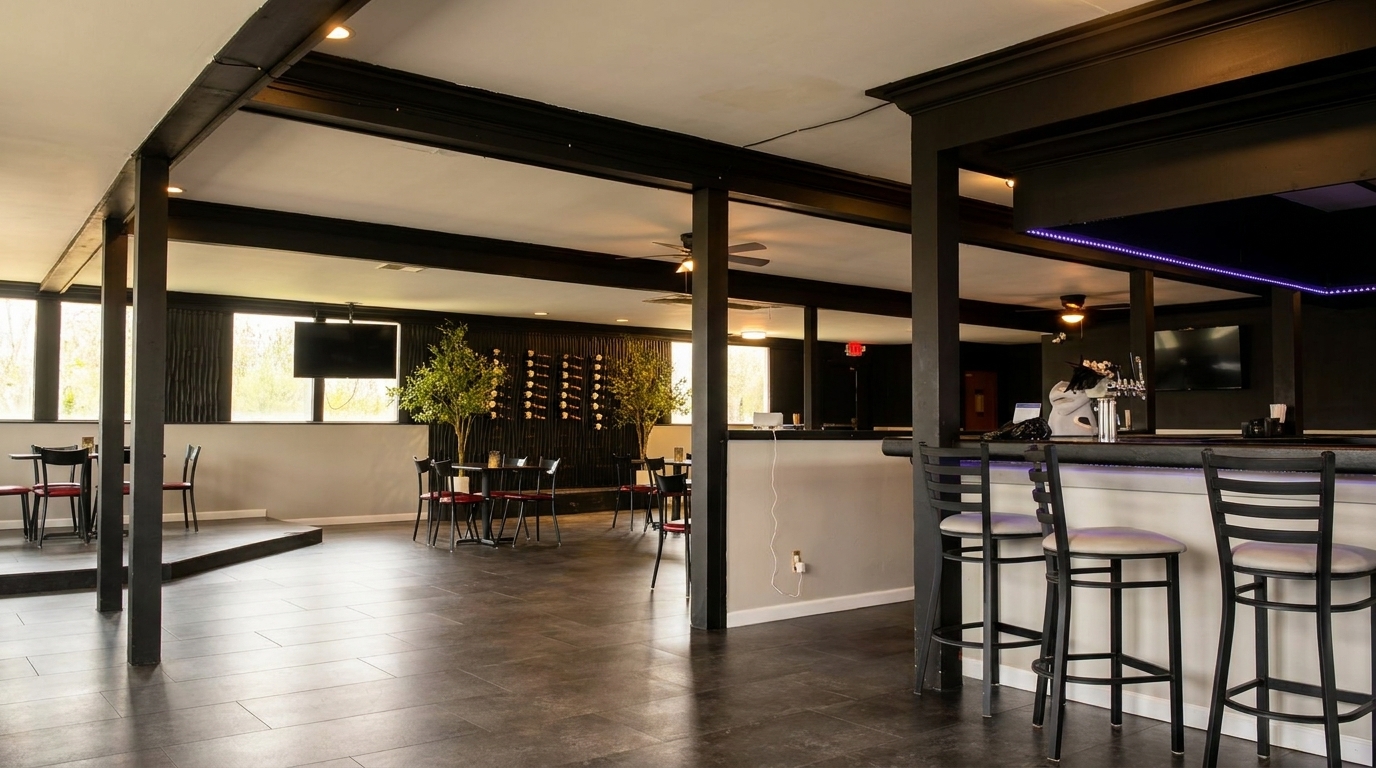 Modern restaurant interior with a bar, high-top tables, and large windows overlooking greenery.