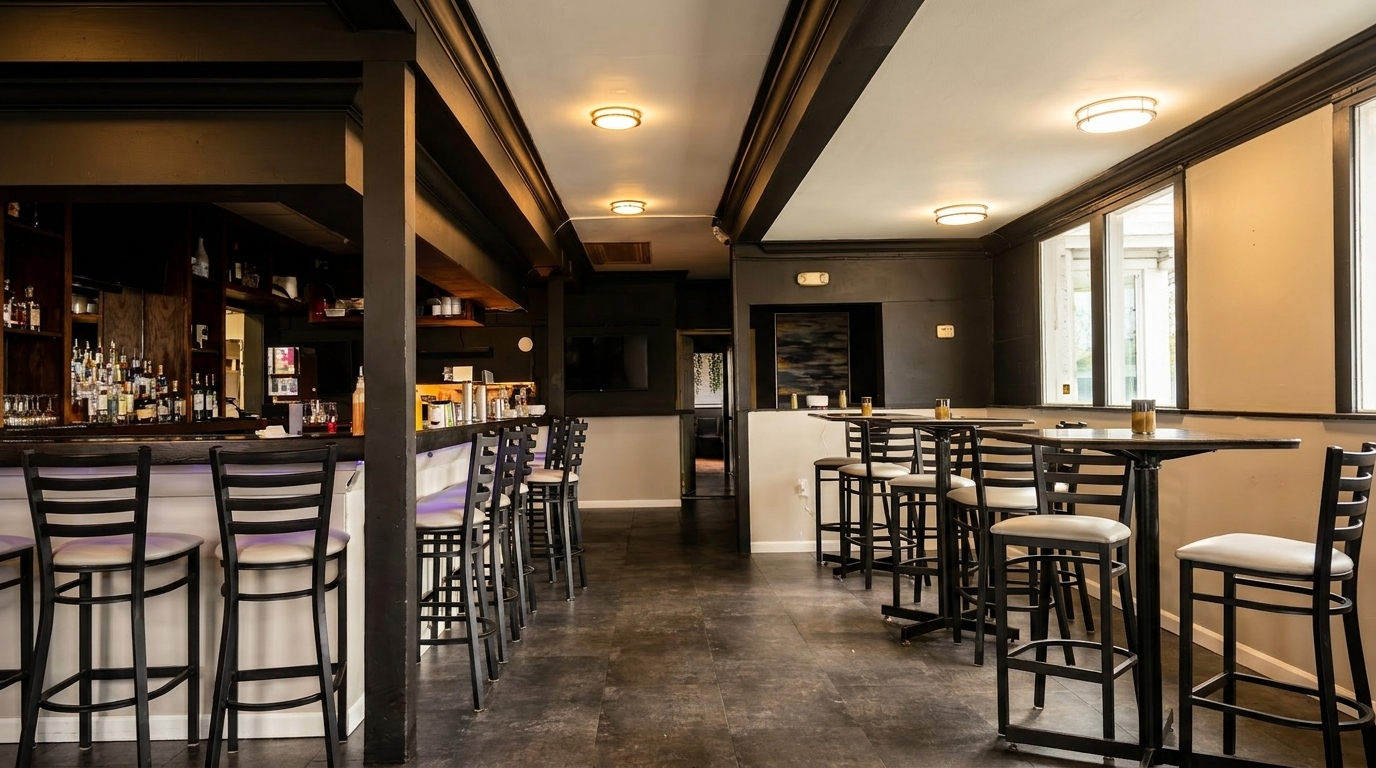 A long, dark bar with stools and high-top tables with chairs in a dimly lit restaurant.