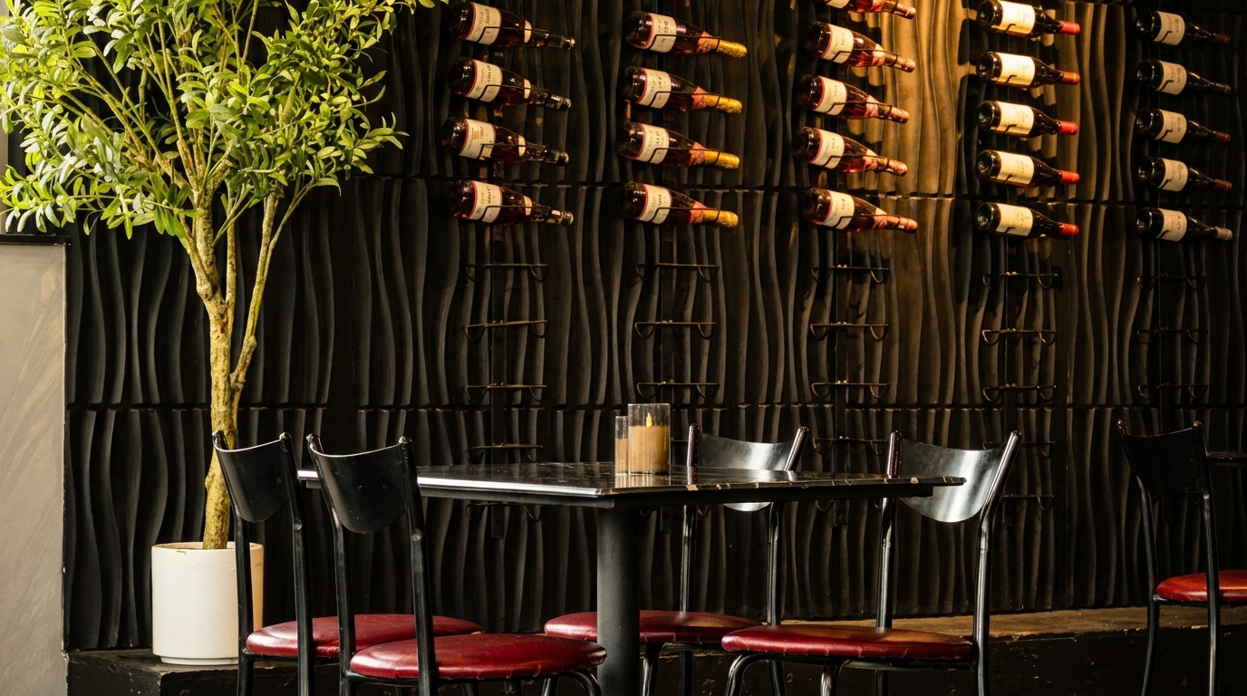 Restaurant interior with a table, chairs, potted plant, and wine bottles on a textured dark wall.