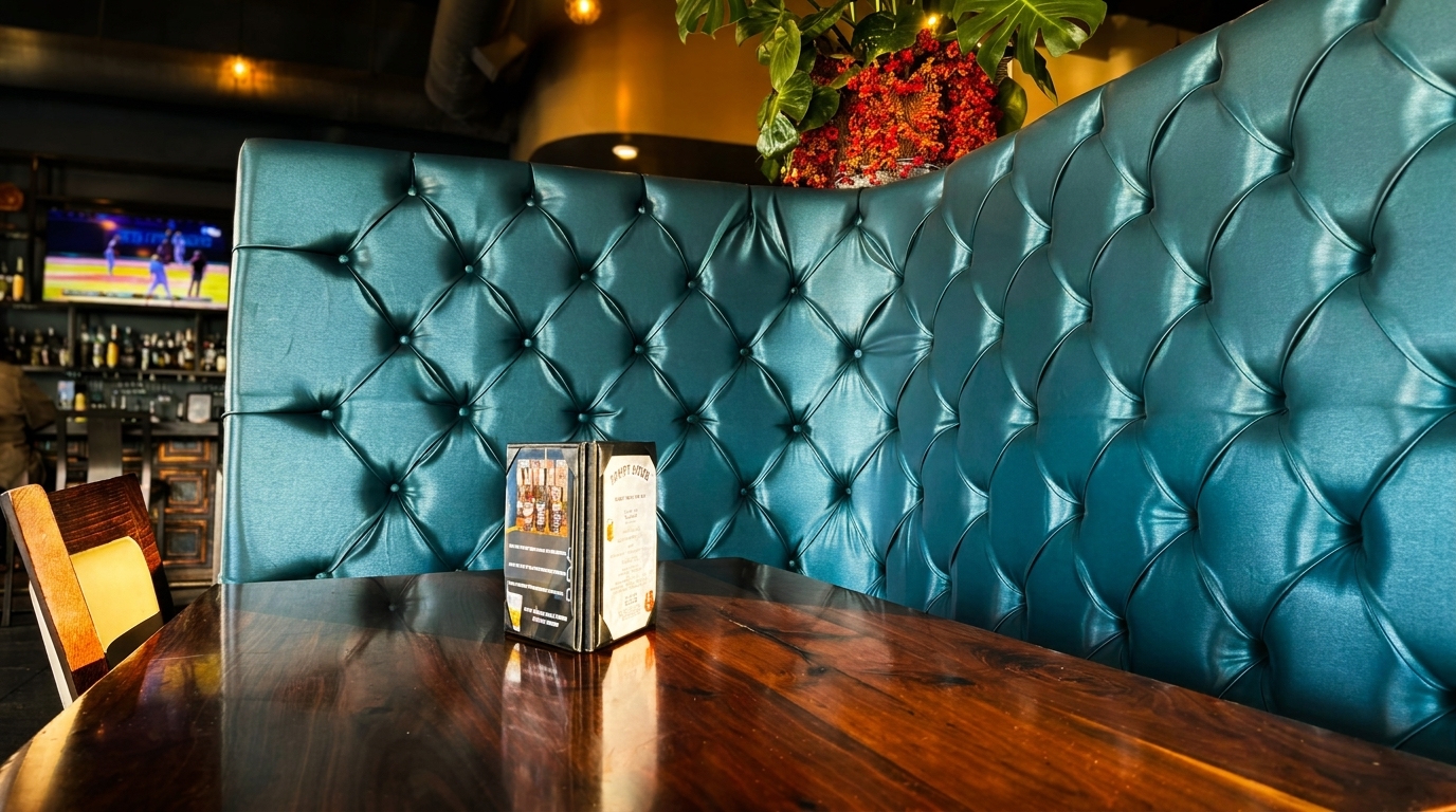 Tufted teal booth seating and a dark wooden table with menus in a restaurant, bar in background.