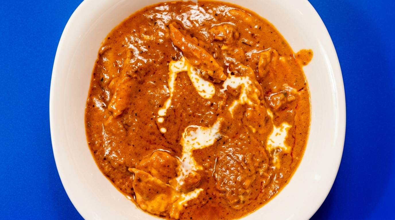 Overhead view of a white bowl filled with chicken tikka masala, garnished with cream swirls.