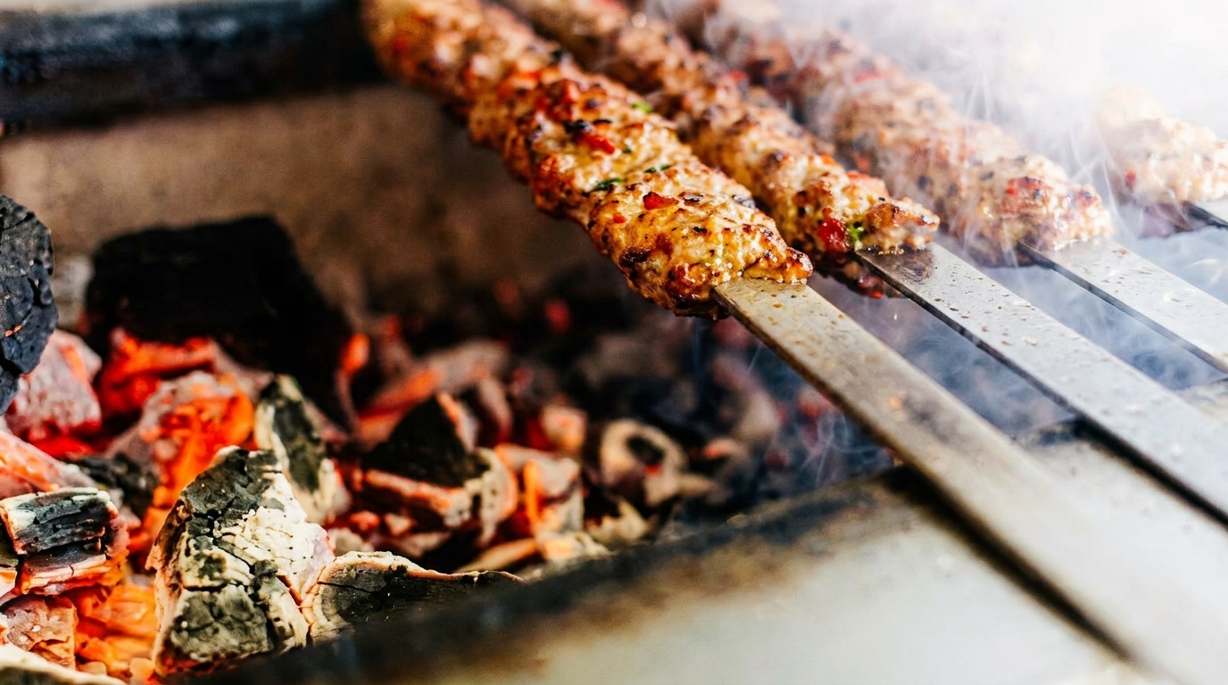 Three skewers of meat kebabs grilling over hot coals with smoke rising.