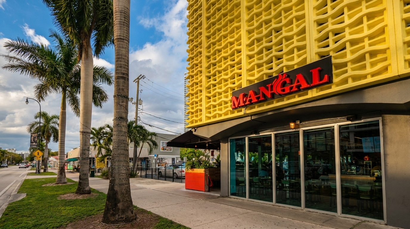 Mangal restaurant exterior with a bright yellow building, palm trees, and a street view.