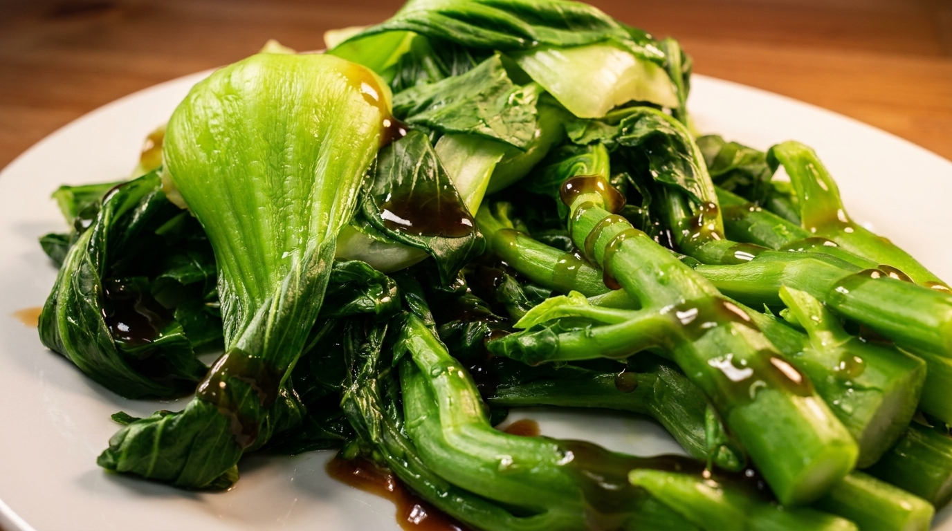 Steamed green bok choy and Chinese broccoli drizzled with a dark sauce on a white plate.