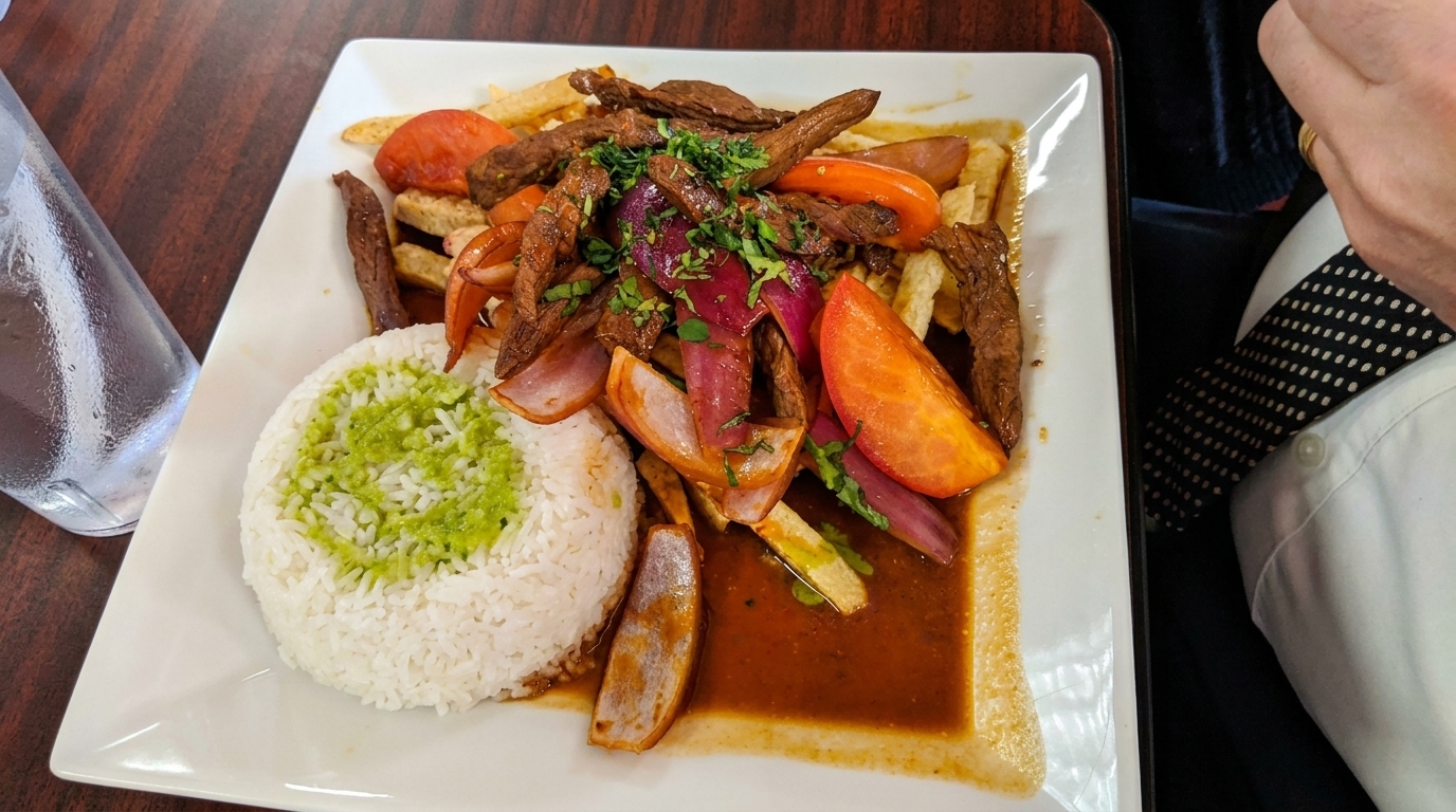 Peruvian Lomo Saltado with steak, fries, tomatoes, red onion, and rice with green sauce.
