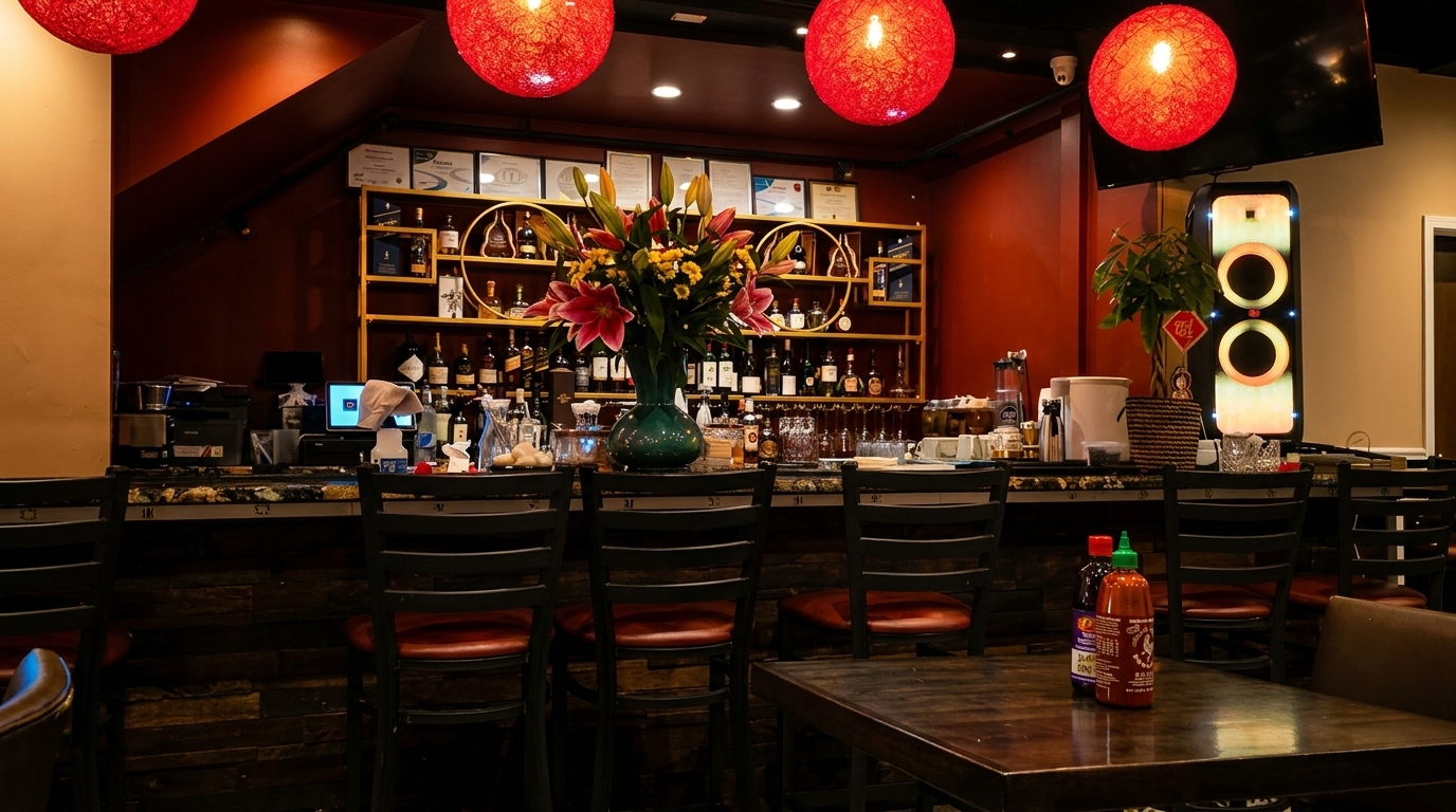 A restaurant bar with red lanterns, a large floral arrangement, and liquor bottles on shelves.