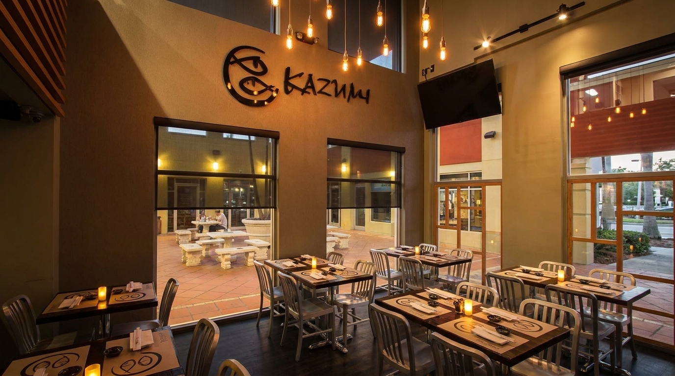Interior of Kazumi restaurant with dining tables, chairs, and large windows overlooking an outdoor patio.