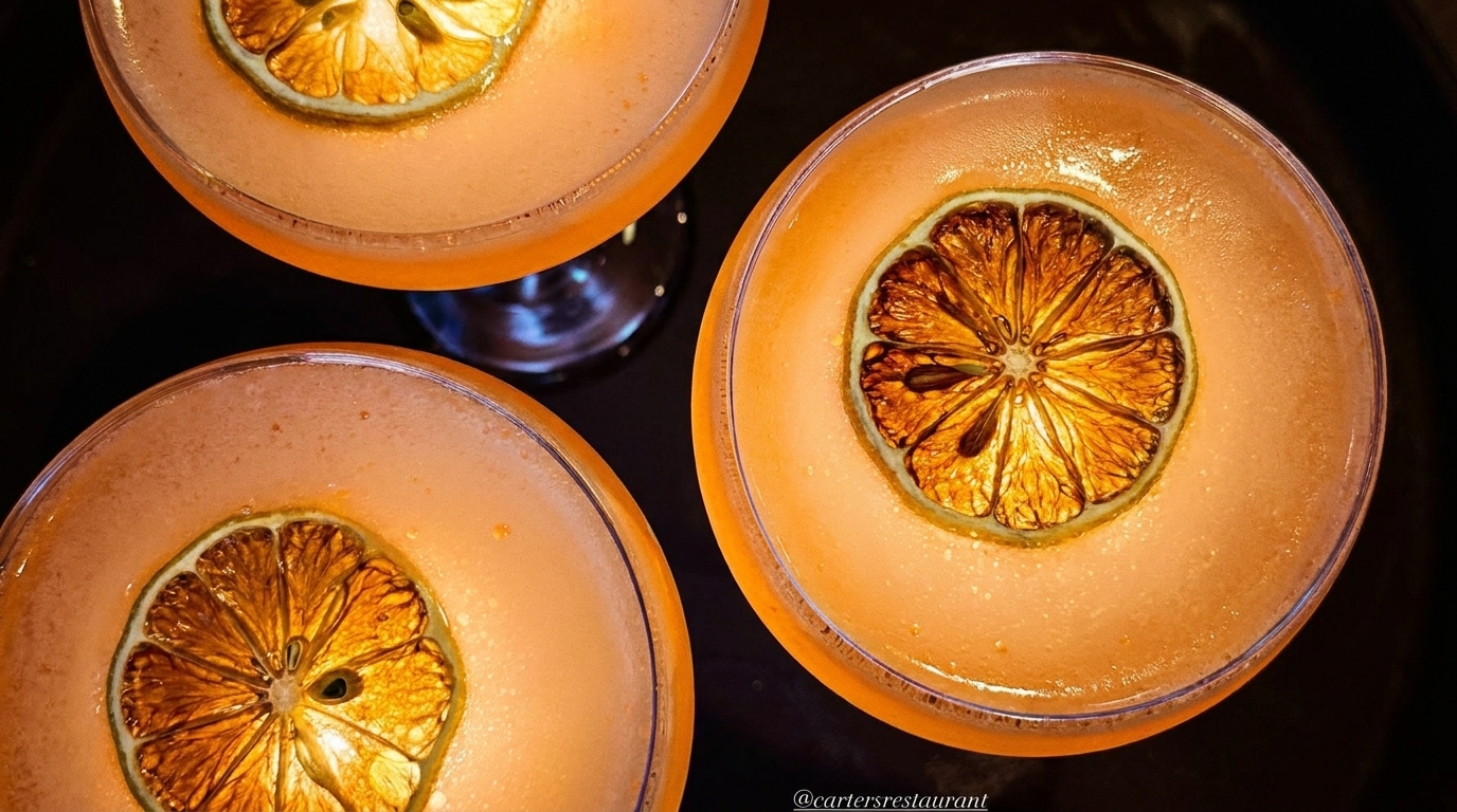 Three orange cocktails in martini glasses, each garnished with a dried citrus slice.