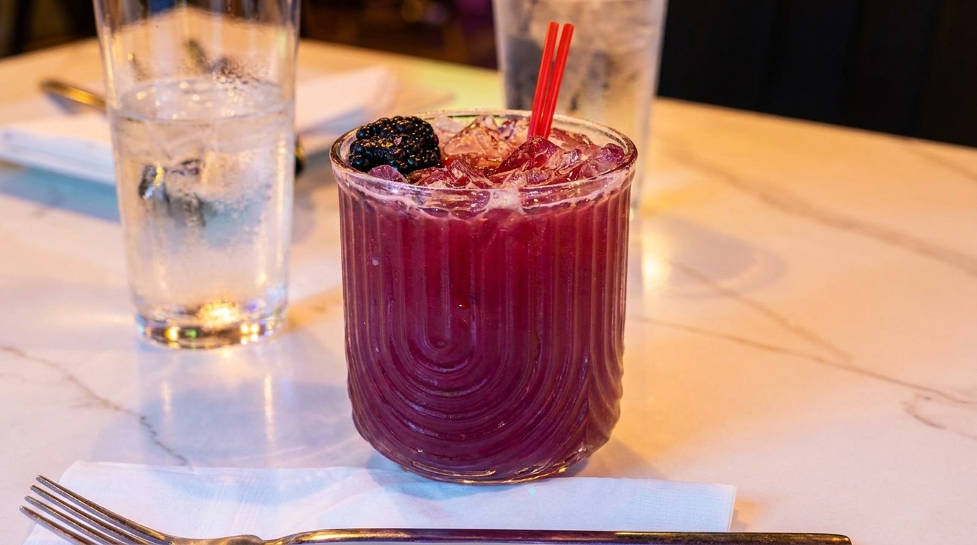 A vibrant red cocktail with ice and a blackberry garnish, next to a glass of water.