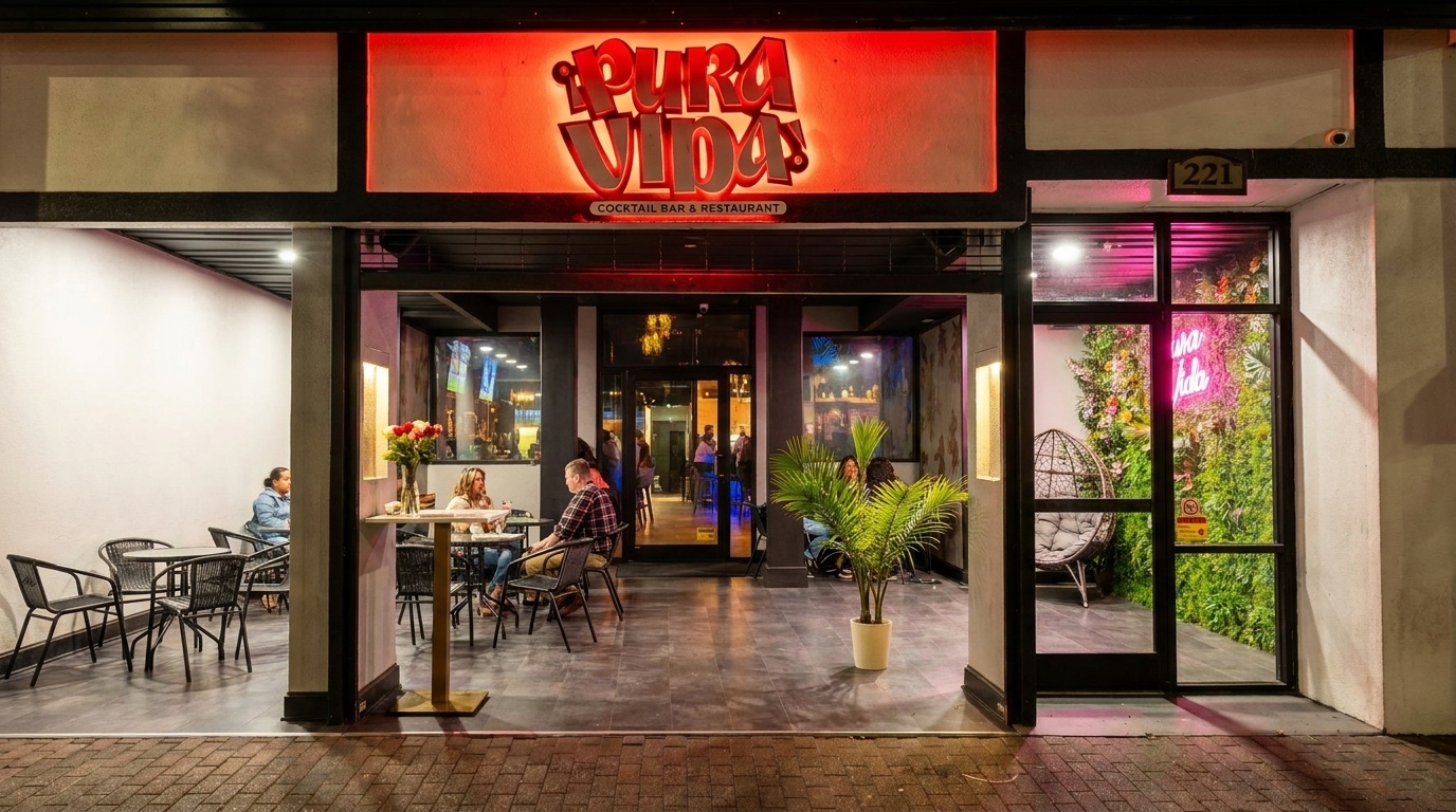 Pura Vida restaurant exterior at night, with a red neon sign, outdoor seating, and patrons.
