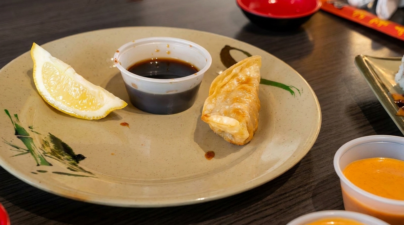 A fried dumpling, soy sauce, and lemon wedge on a plate with bamboo art.