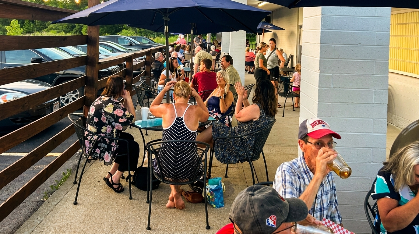 Patrons enjoy outdoor dining under blue umbrellas at a restaurant patio next to a parking lot.