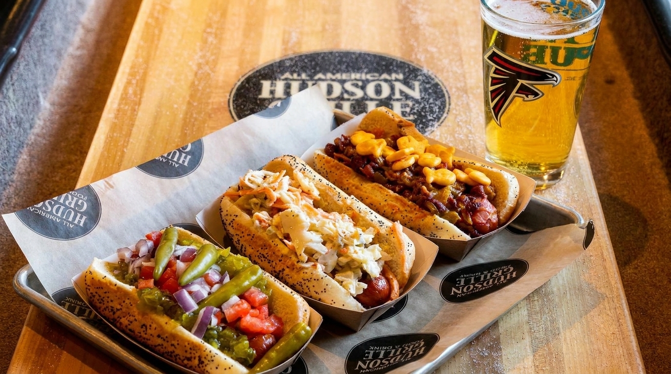 Three gourmet hot dogs with various toppings and a glass of beer on a wooden table.