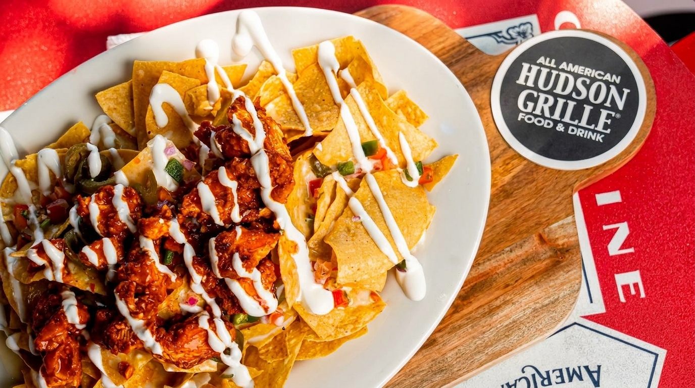 A plate of Hudson Grille nachos with chicken, jalapeños, and white sauce on a wooden board.