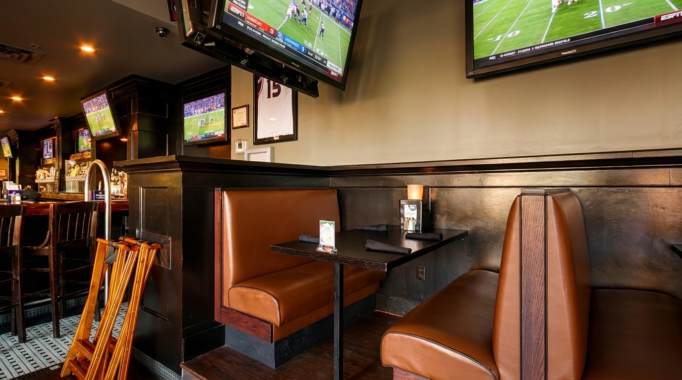 Cozy restaurant interior with brown booths, dark tables, and multiple TVs showing sports above.