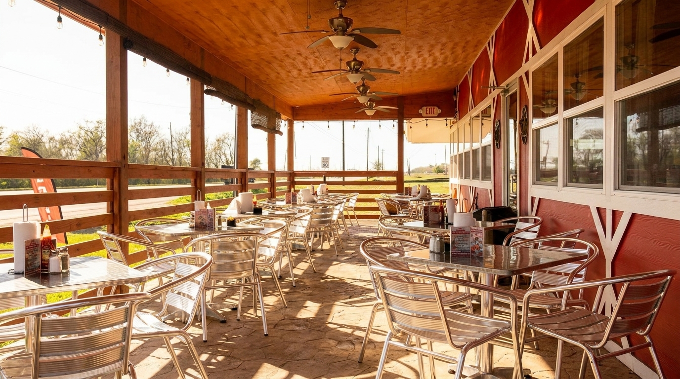 Outdoor patio dining area with metal tables and chairs, ceiling fans, and a red building exterior.