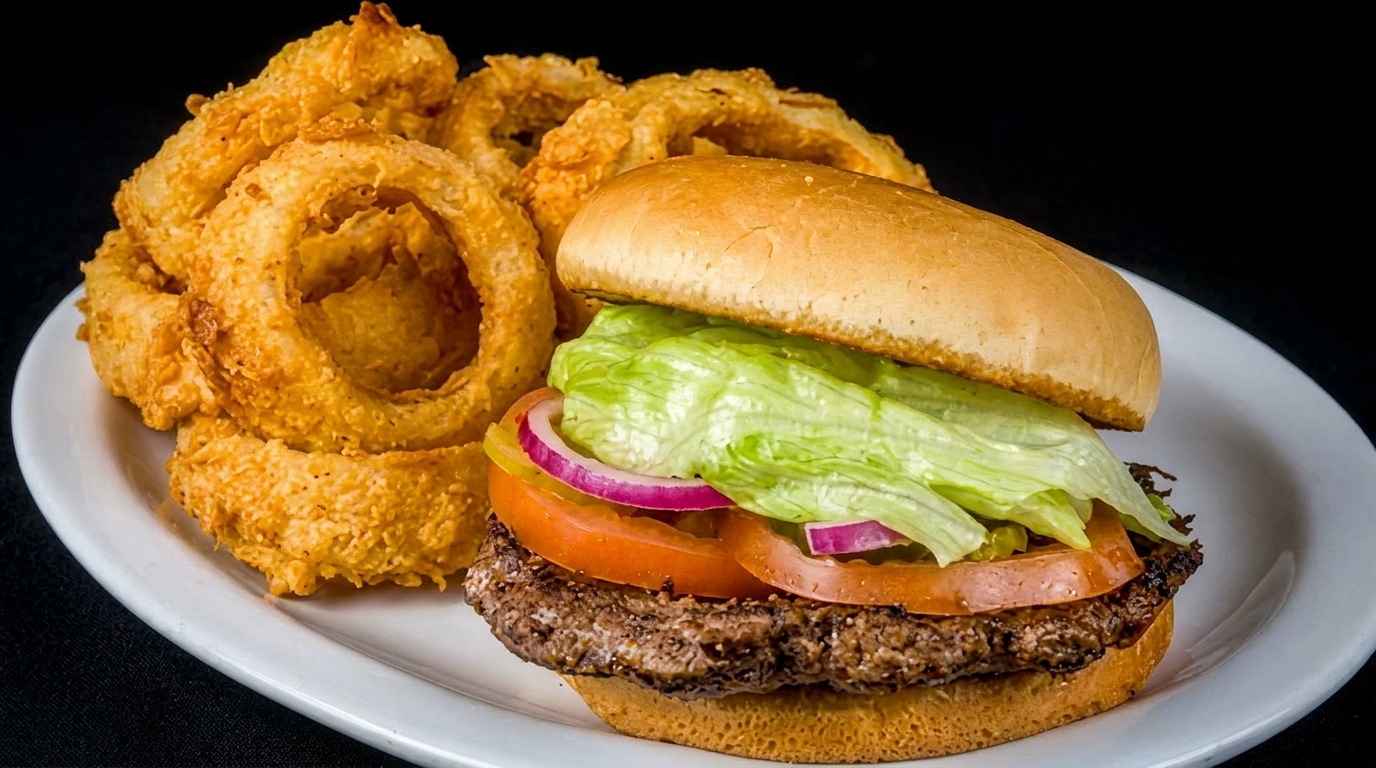 A juicy hamburger with lettuce, tomato, and onion, served with a side of crispy onion rings.