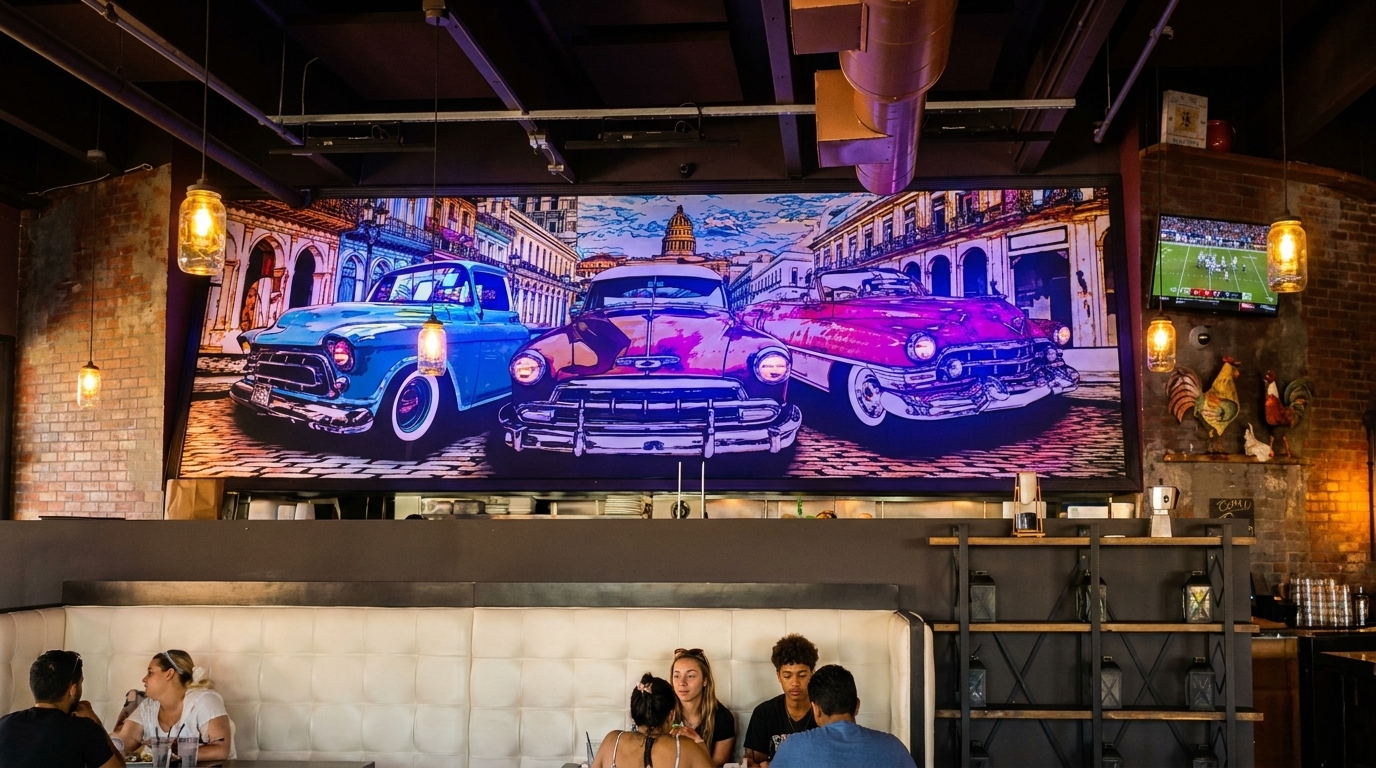Restaurant interior with a large mural of vintage cars, people dining, and brick walls with decor.