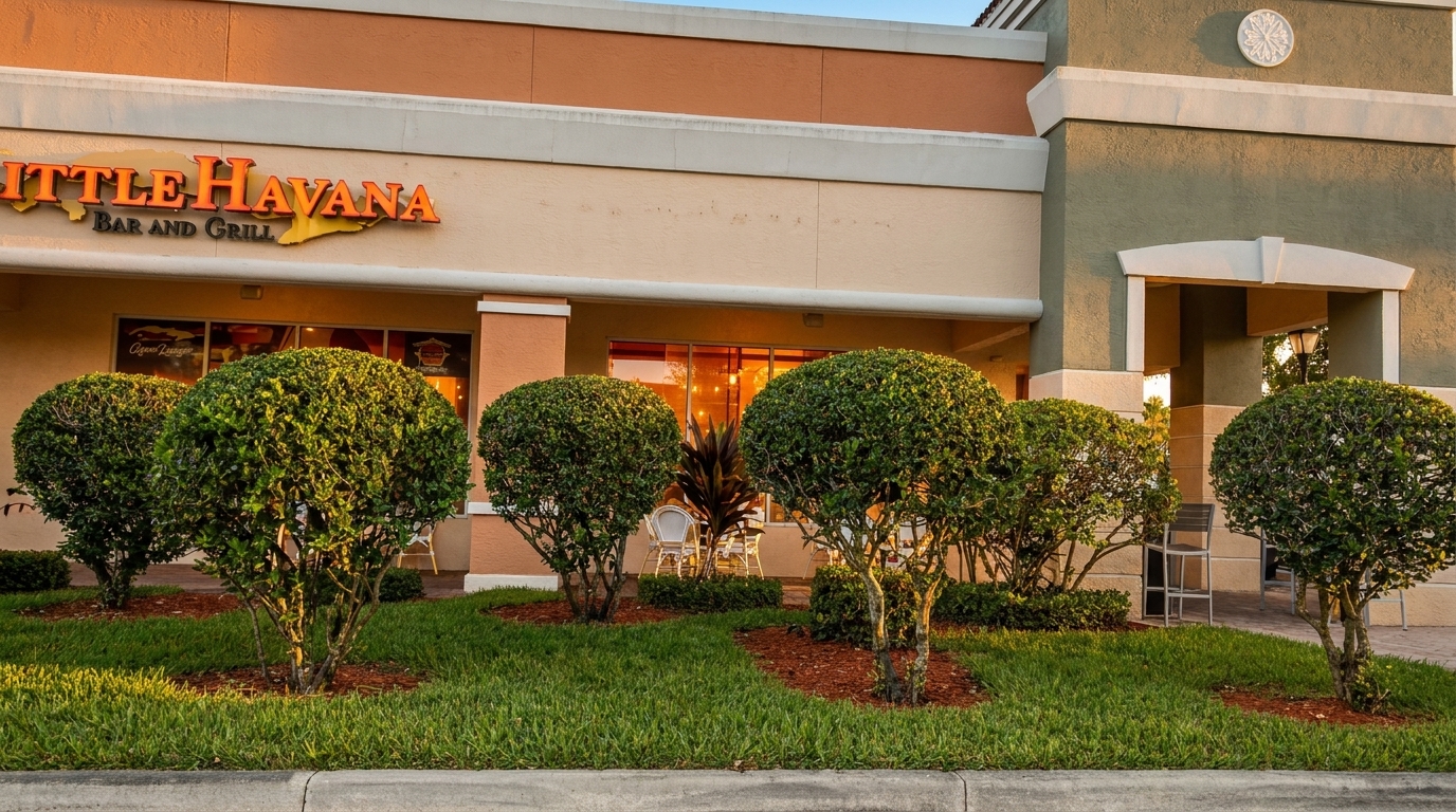 Exterior of Little Havana Bar and Grill with green bushes, grass, and warm interior lighting.