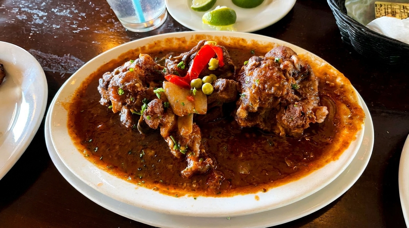 Oxtail stew with red peppers, peas, and potatoes in a rich brown sauce on a white plate.