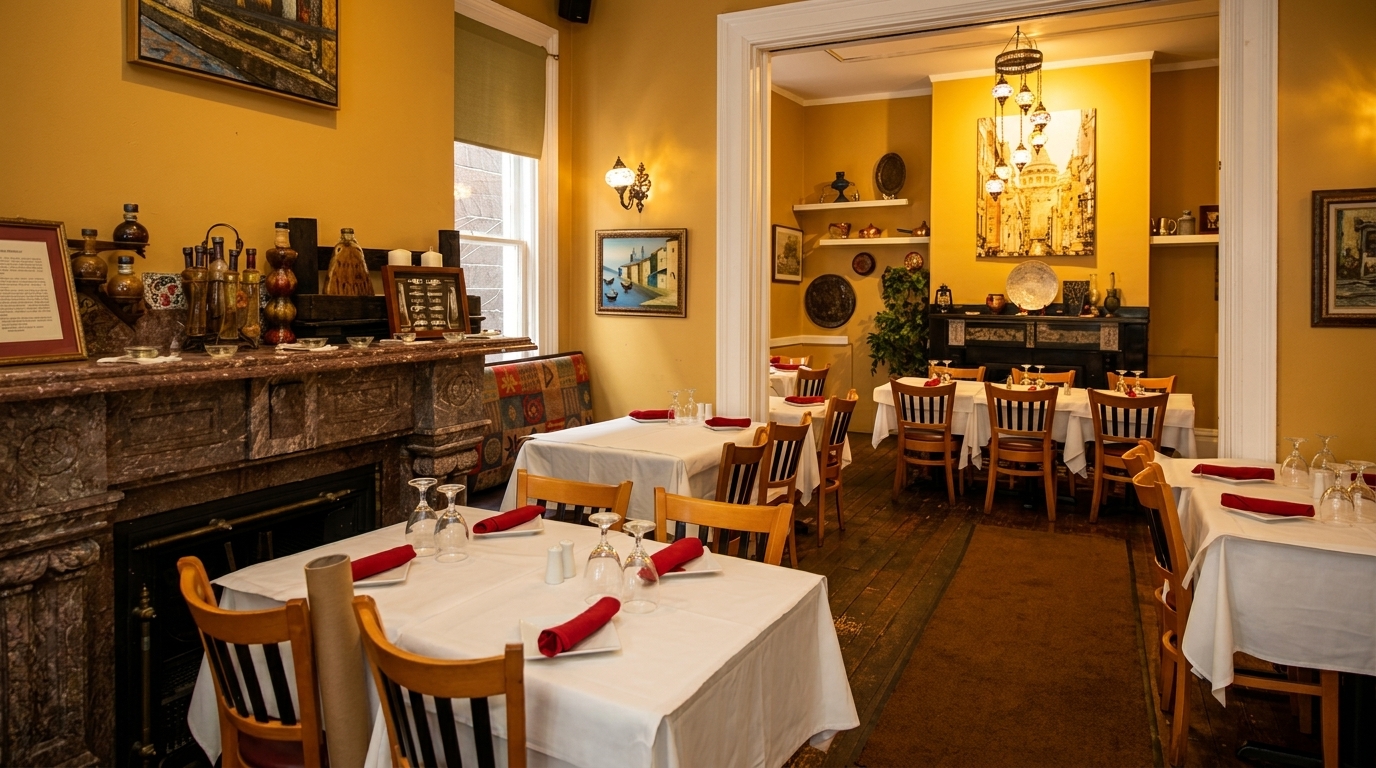 A warmly lit restaurant dining room with white tablecloths, red napkins, and decorative art on mustard-yellow walls.