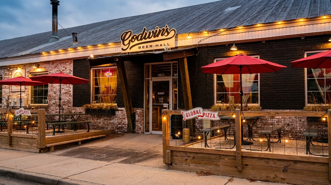 Godwin's Beer Hall exterior with outdoor patio seating, red umbrellas, and string lights at dusk.