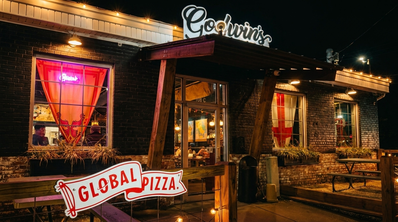 Godwin's Global Pizza restaurant exterior at night, with illuminated sign and outdoor seating.