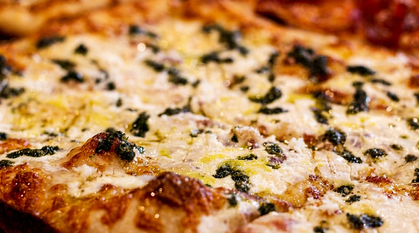 Close-up of a freshly baked pizza with melted cheese, green pesto, and a golden-brown crust.