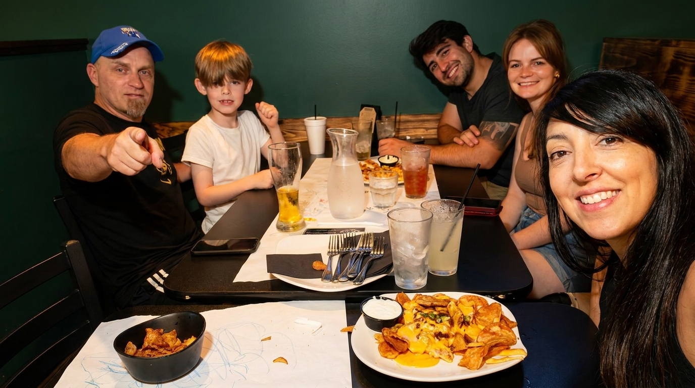 A family of five smiles at the camera while seated around a restaurant table with food and drinks.