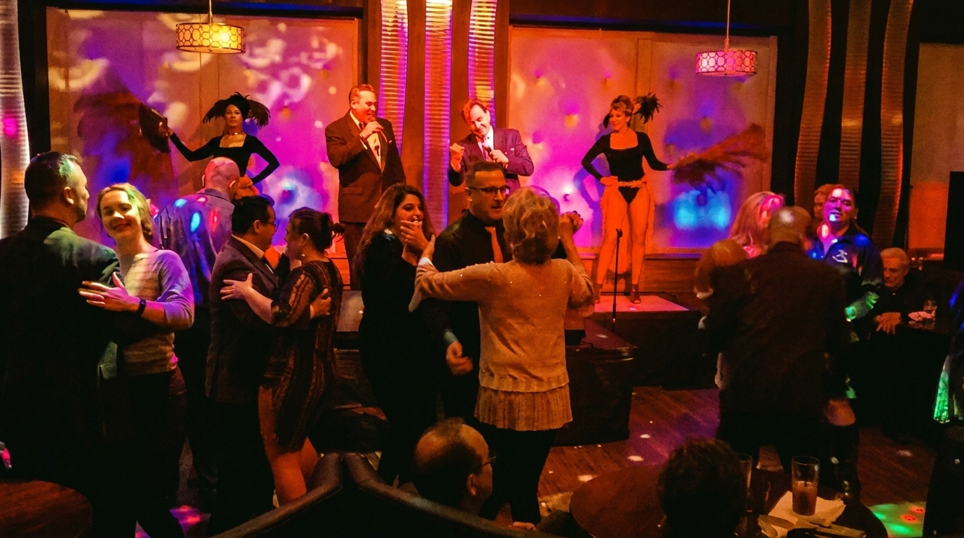 People dancing and enjoying live entertainment with singers and showgirls on a stage.