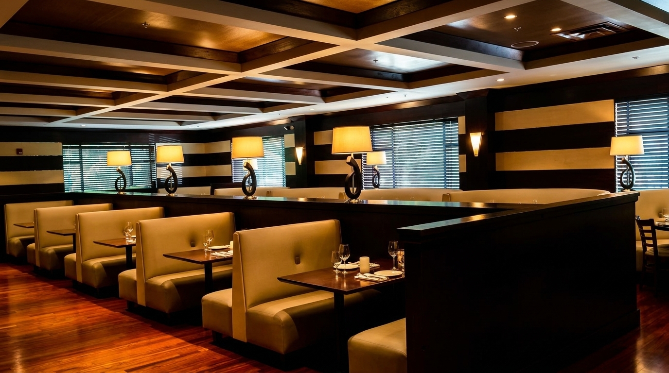 Warmly lit restaurant interior with rows of beige booths, dark wood tables, and decorative lamps.