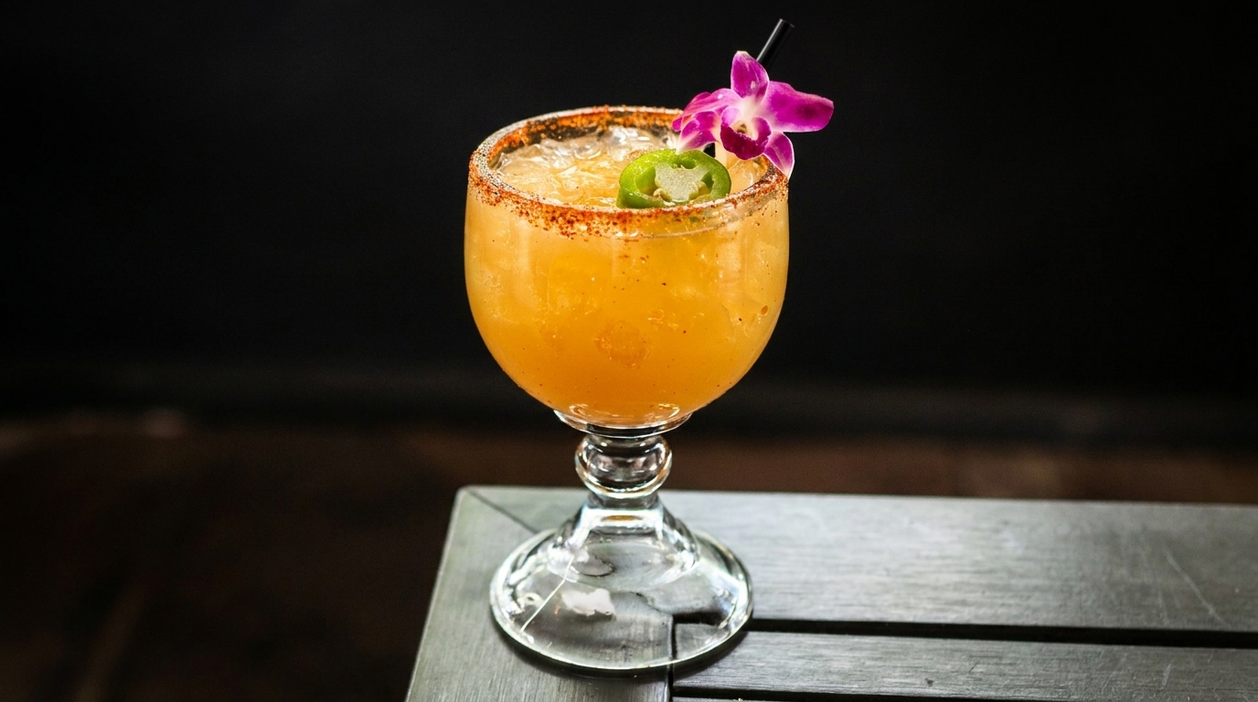 Spicy orange cocktail with a chili-salted rim, jalapeño slice, and purple orchid garnish.