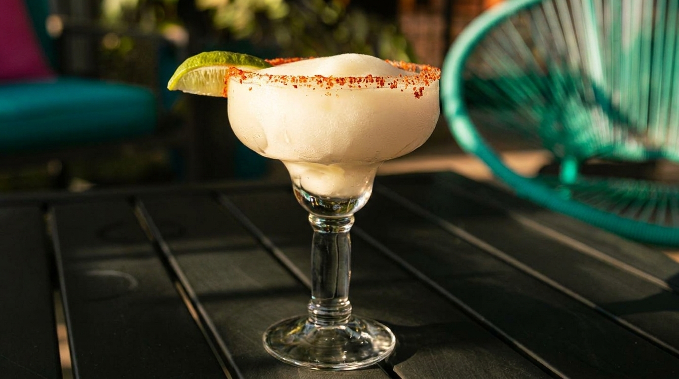 Frozen margarita with a chili-salt rim and lime wedge on a dark patio table.