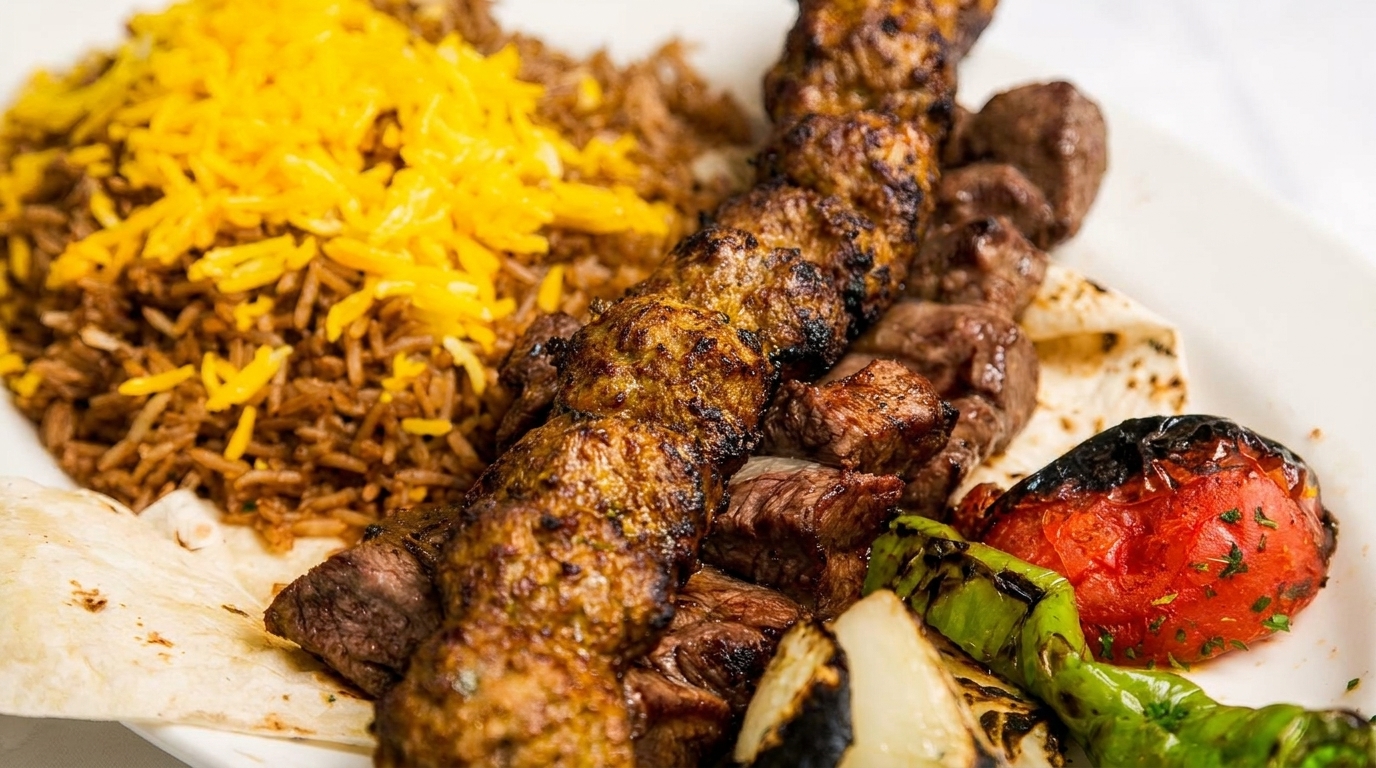 Two skewers of grilled meat, rice, flatbread, and roasted vegetables on a white plate.