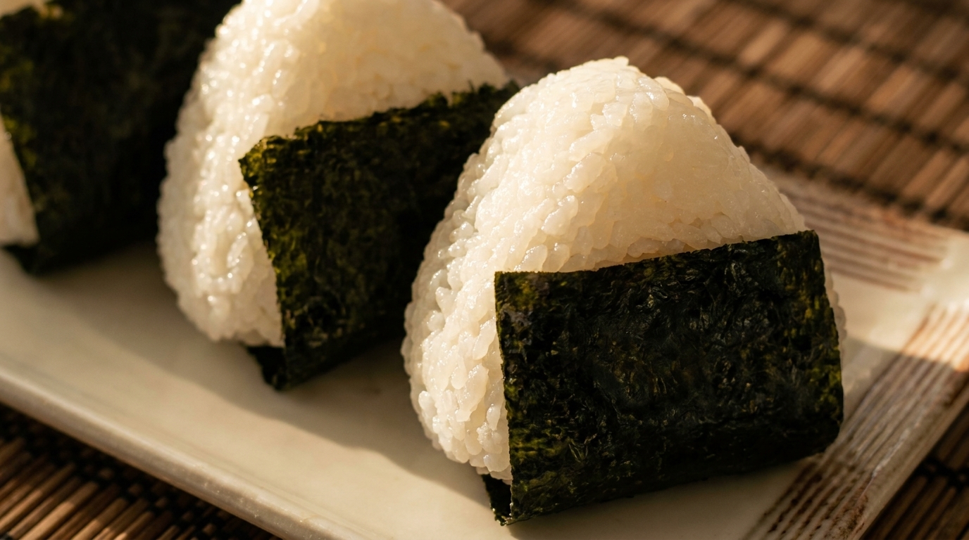 Three triangular onigiri rice balls wrapped in nori seaweed, on a white plate.