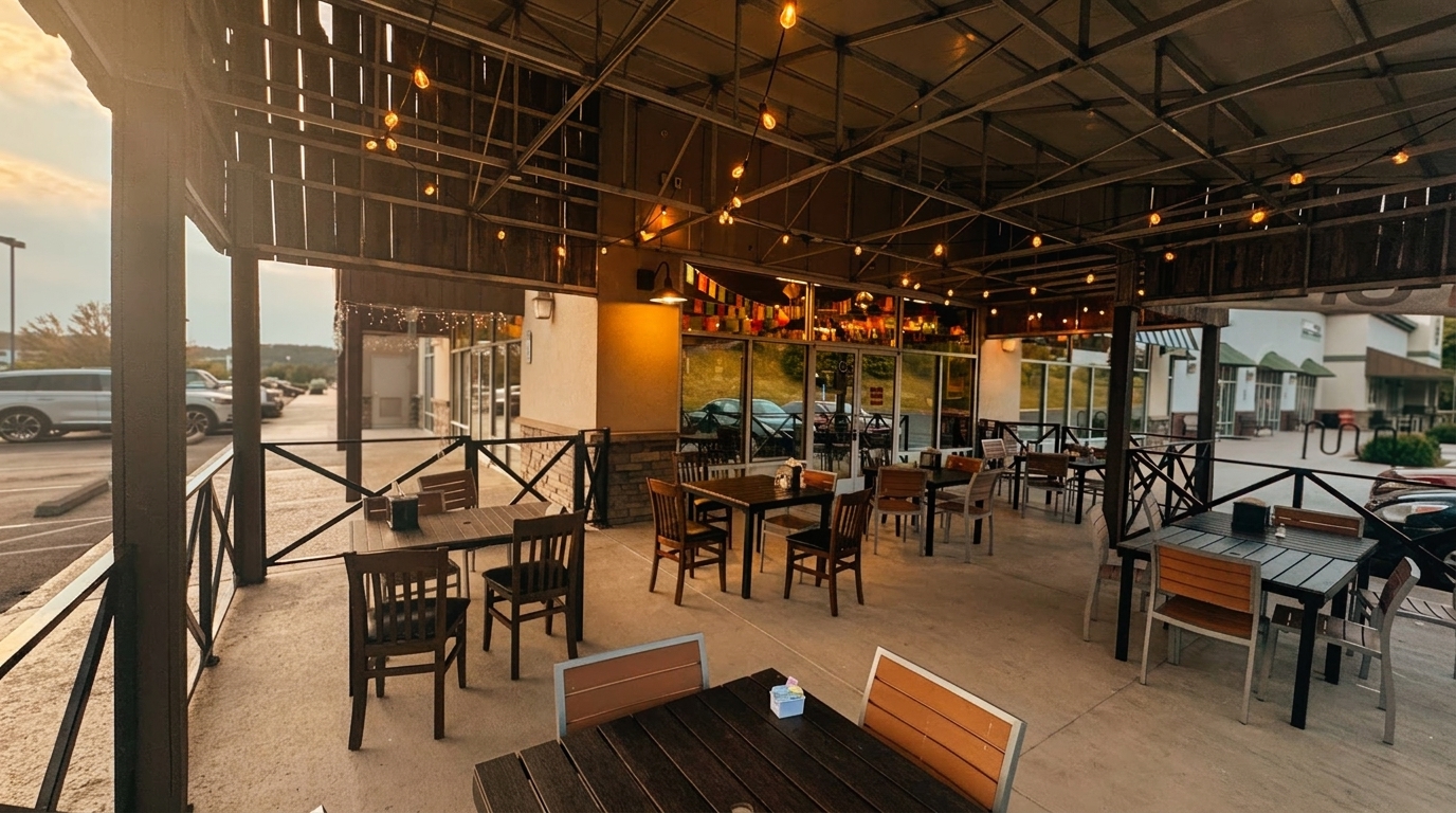 An empty restaurant patio with wooden tables and chairs under a string-lit canopy at dusk.