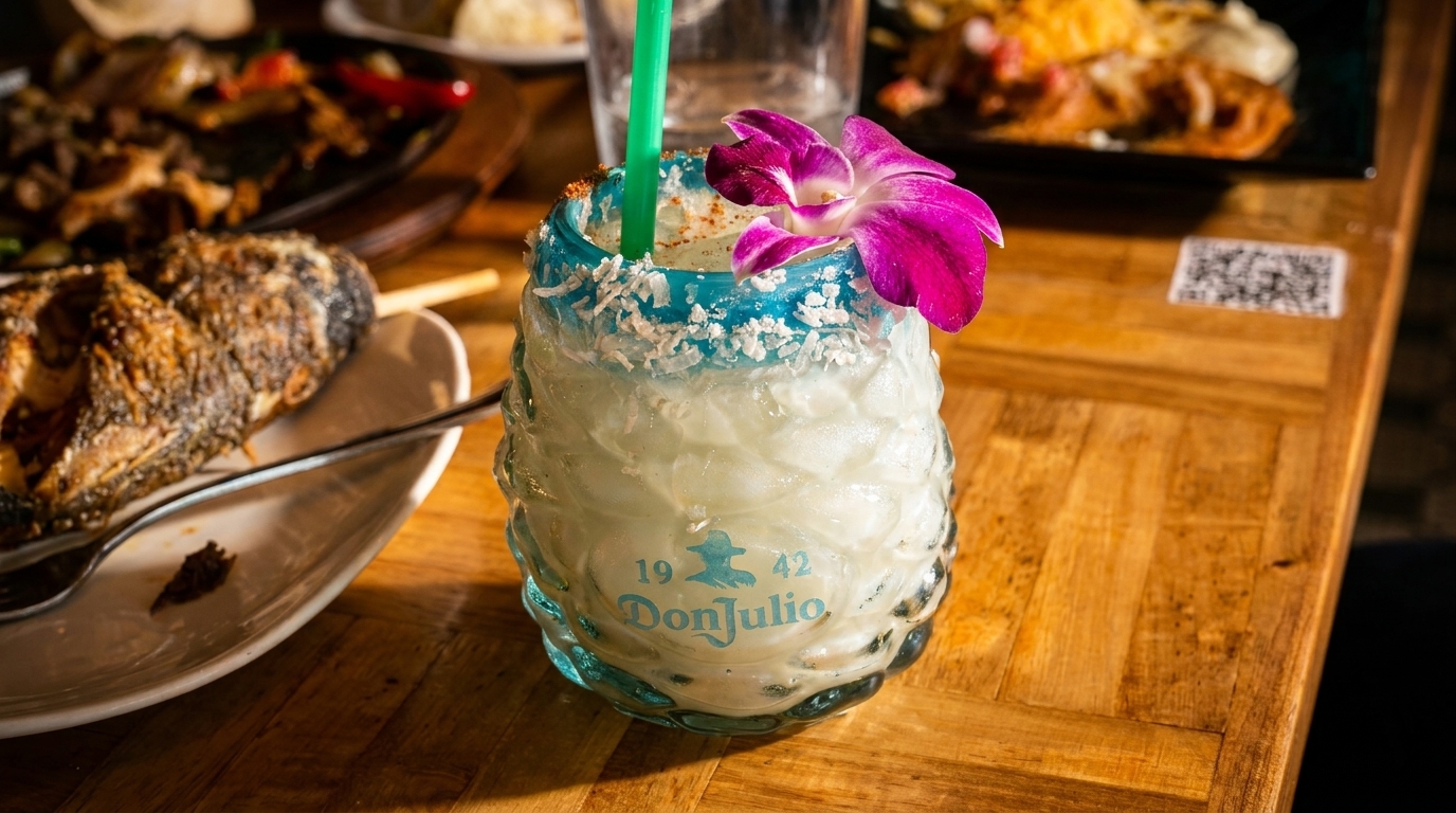 A Don Julio cocktail with a purple orchid garnish and coconut rim sits on a wooden table.
