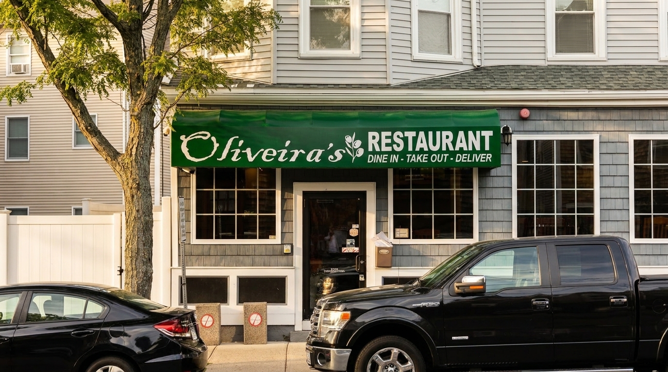 Oliveira's Restaurant storefront with a green awning, two cars parked in front, and a tree.