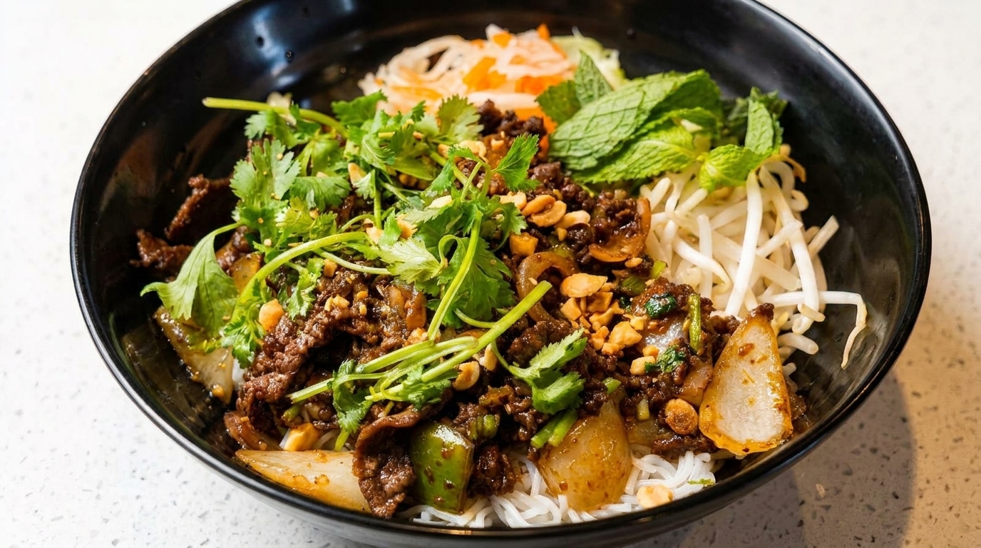 A close-up of a Vietnamese vermicelli bowl with beef, herbs, peanuts, and bean sprouts.